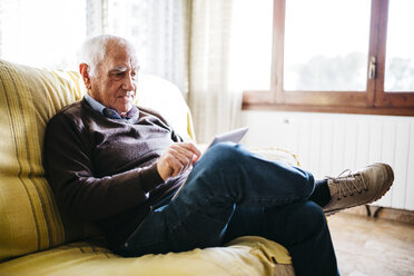 Älterer Mann sitzt auf der Couch und benutzt ein Tablet - JRFF01066