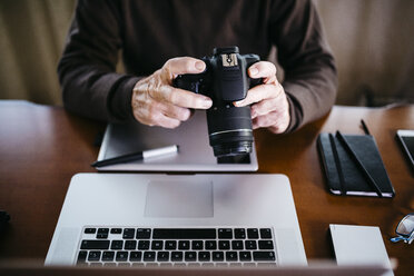 Senior photographer with laptop and digital camera at home, partial view - JRFF01068