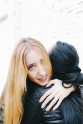 Portrait of young woman hugging her friend in front of white brick wall - GEMF01282