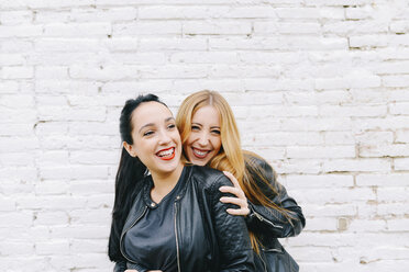Zwei lachende junge Frauen vor einer weißen Backsteinmauer - GEMF01285