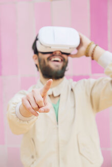 Lächelnder Mann mit Virtual-Reality-Brille vor der rosa Wand - RTBF00535