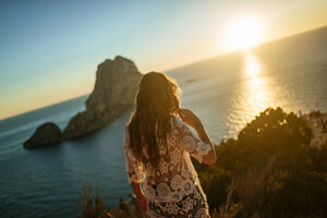 Spanien, Ibiza, Frau mit Blick auf das Meer und die Insel Es Vedra bei Sonnenuntergang - KIJF01022