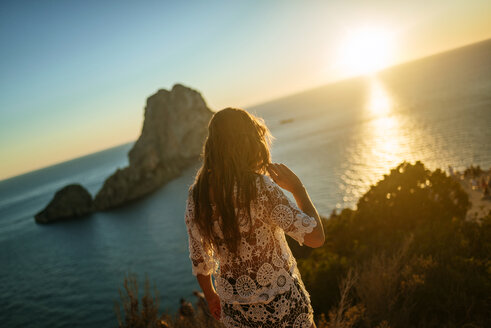 Spain, Ibiza, Woman looking at the sea and Es Vedra island at sunset - KIJF01022