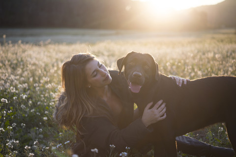 Junge Frau und ihr Hund in einem Blumenfeld in der Dämmerung, lizenzfreies Stockfoto