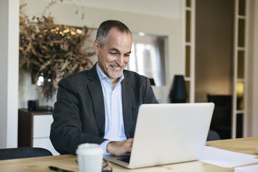 Erfolgreicher Geschäftsmann sitzt am Schreibtisch und arbeitet am Laptop - EBSF01905