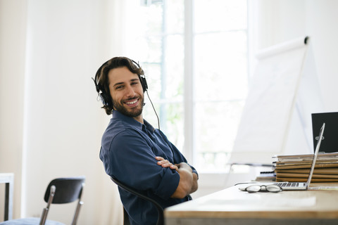 Geschäftsmann im Büro mit Kopfhörern am Schreibtisch, lizenzfreies Stockfoto