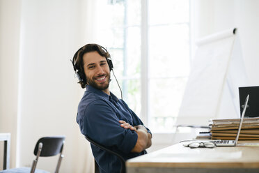 Businessman in office using headphones at desk - EBSF01943