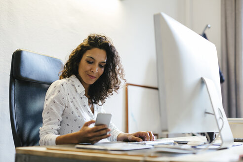 Erfolgreiche Geschäftsfrau sitzt im Büro und hält ein Smartphone in der Hand - EBSF01959