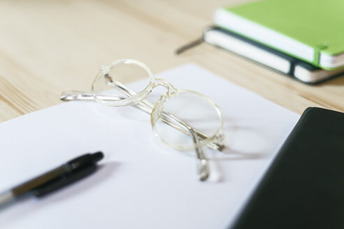 Brille auf einem Blatt Papier auf dem Schreibtisch mit Notizbuch und Stift - EBSF01962