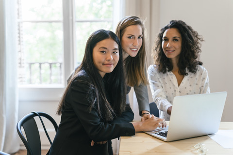 Drei Geschäftsfrauen arbeiten gemeinsam an einem Laptop, lizenzfreies Stockfoto