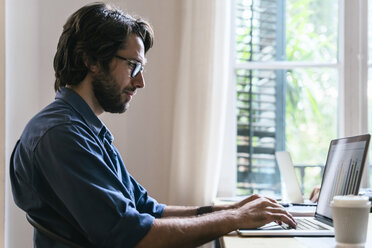 Geschäftsmann sitzt im Büro und arbeitet am Laptop - EBSF02000