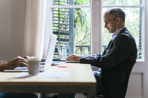 Geschäftsmann sitzt am Schreibtisch und arbeitet am Laptop, lizenzfreies Stockfoto