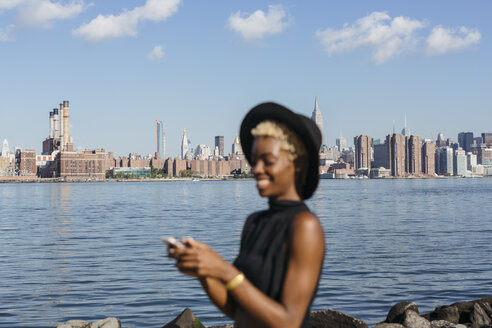 USA, New York City, Brooklyn, lächelnde junge Frau am East River mit der Skyline von Manhattan im Hintergrund - GIOF01648