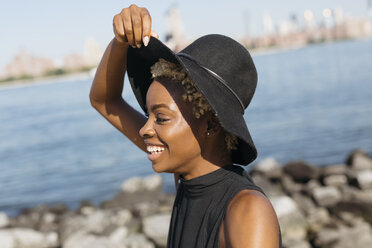 USA, New York City, Brooklyn, smiling young woman at East River wearing a hat - GIOF01652