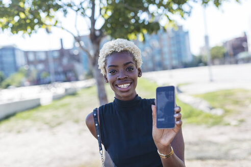 Porträt einer lächelnden jungen Frau, die ihr Mobiltelefon zeigt - GIOF01655