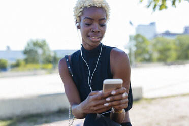 Smiling young woman with cell phone and earbuds - GIOF01661