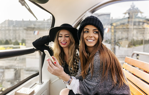 Frankreich, Paris, zwei lächelnde Frauen mit Mobiltelefon in einem Reisebus, lizenzfreies Stockfoto