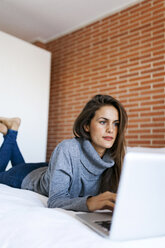 Junge Frau auf dem Bett liegend mit Laptop - VABF00854