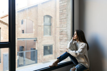 Young woman sitting at a window looking out - VABF00866