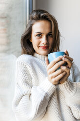 Smiling young woman drinking a coffee at a window - VABF00869