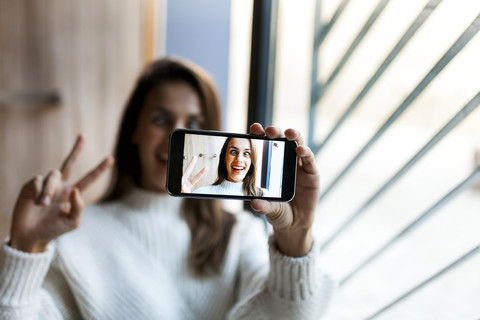 Verspielte junge Frau macht ein Selfie mit Handy, lizenzfreies Stockfoto