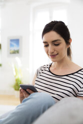 Smiling woman at home looking on cell phone - FKF02076