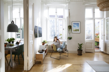 Woman at home sitting on chair talking on cell phone - FKF02079