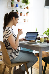 Lächelnde Frau zu Hause, die am Tisch sitzt und einen Laptop benutzt - FKF02082