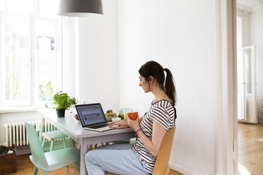 Frau zu Hause am Tisch sitzend mit Laptop - FKF02084