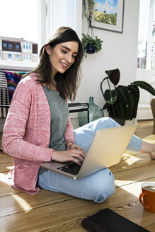 Frau zu Hause auf dem Boden sitzend mit Laptop - FKF02093