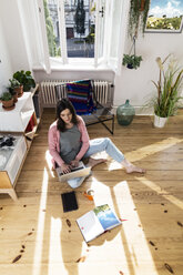 Woman at home sitting on floor using laptop - FKF02094