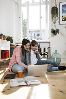 Mutter und Tochter sitzen zu Hause auf dem Boden und benutzen einen Laptop - FKF02095