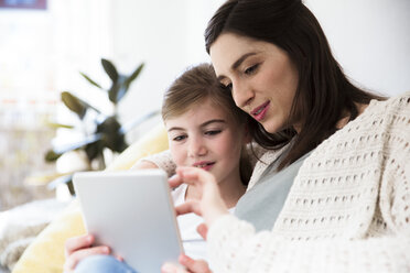 Smiling mother and daughter at home using tablet - FKF02107