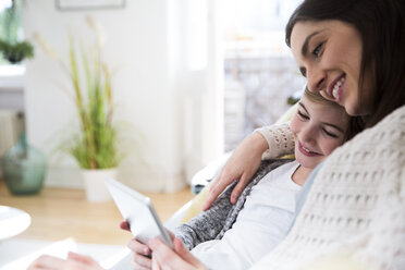 Smiling mother and daughter at home using tablet - FKF02108