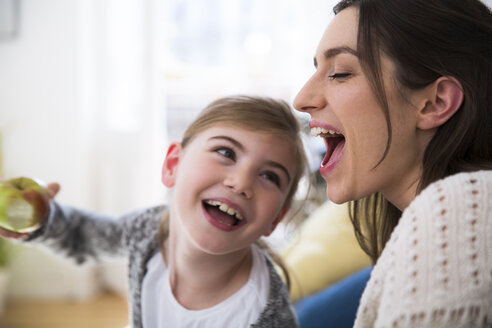 Glückliche Mutter und Tochter essen einen Apfel zu Hause - FKF02110