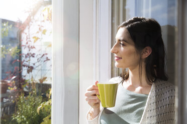 Lächelnde Frau mit einer Tasse Kaffee in der Hand am Fenster - FKF02114