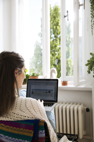 Woman at home using laptop at the window stock photo