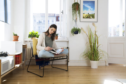 Frau zu Hause auf einem Stuhl sitzend und ein Buch lesend - FKF02120