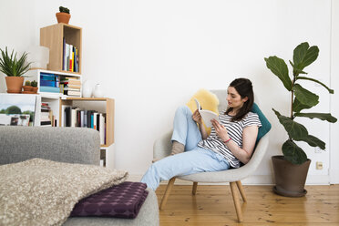 Frau zu Hause auf einem Stuhl sitzend und ein Buch lesend - FKF02126