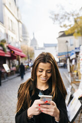 Frankreich, Paris, junge Frau schaut auf Handy in Montmartre - MGOF02649