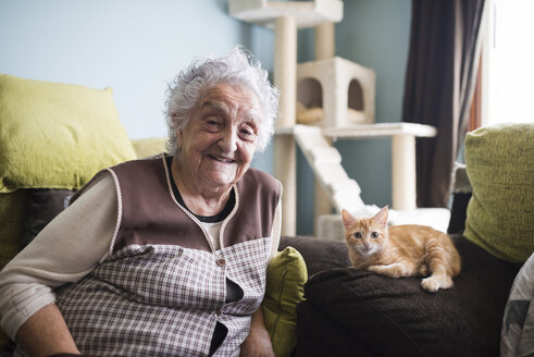 Porträt einer glücklichen Frau und ihrer Katze, die auf der Couch im Wohnzimmer sitzen - RAEF01591