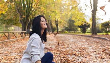 Glückliche junge Frau spielt mit Blättern in einem Park im Herbst - MGOF02656