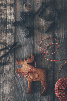 Elk-shaped cookie, cookie cutter, scissors and string on dark wood - RTBF00537