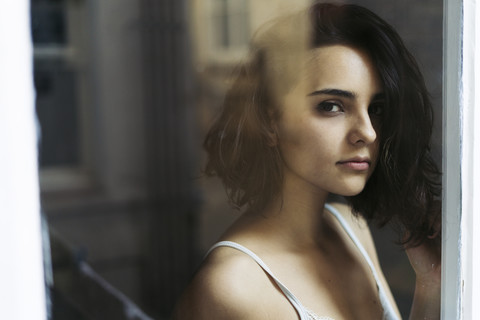 Porträt einer jungen Frau, die durch ein Fenster schaut, lizenzfreies Stockfoto