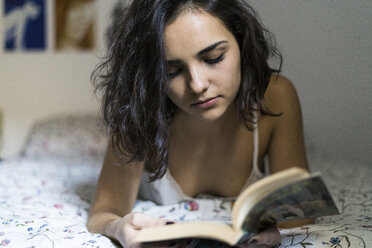 Young woman lying on bed reading a book - KKAF00151