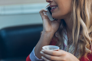 Smiling woman with takeaway coffee talking on cell phone, close-up - ZEDF00445