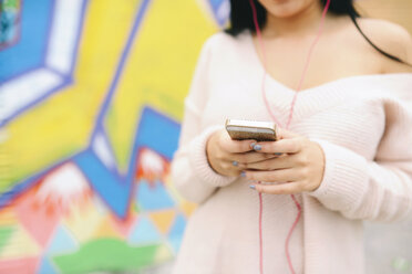 Hands of woman holding cell phone in front of graffiti wall - GEMF01291