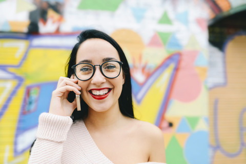 Porträt einer glücklichen Frau am Telefon vor einer Graffitiwand, lizenzfreies Stockfoto