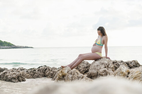 Schwangere Frau sitzt auf einem Felsen am Meer - DIGF01488