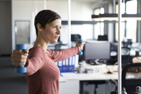 Geschäftsfrau im Büro beim Training mit Hanteln, lizenzfreies Stockfoto